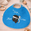 Bavoir bébé personnalisé Mini Corse avec prénom Enzo posé sur une table avec accessoires bébé, création artisanale