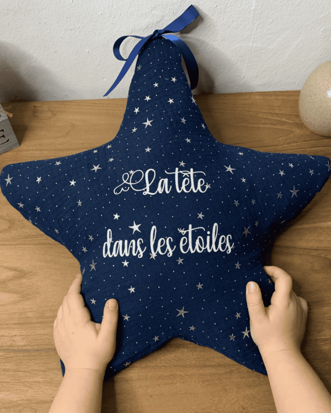 eilleuse étoile personnalisée en tissu bleu nuit avec message "La tête dans les étoiles", tenue par les mains d'un enfant.